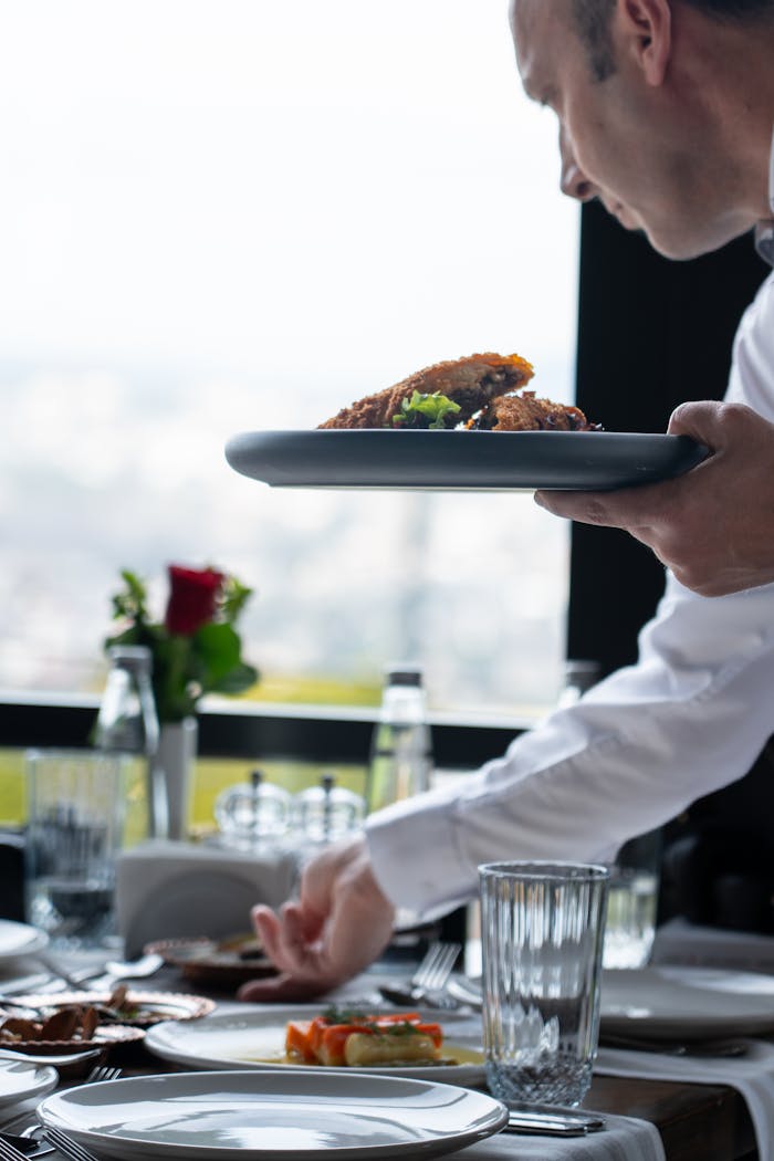 ours-journey A waiter serves gourmet dishes in a sophisticated restaurant setting, enhancing a fine dining atmosphere.