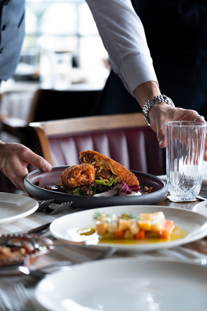 A waiter serves a plate of crispy fried chicken with mixed vegetables at a restaurant table.