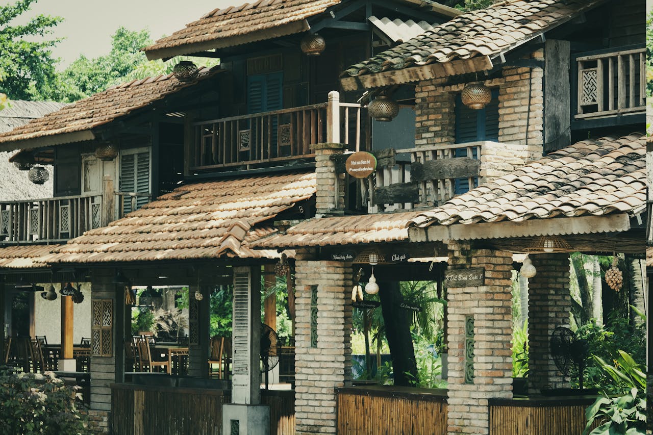 about-02 Charming country inn with rustic brick and wood architecture surrounded by lush greenery on a sunny day.