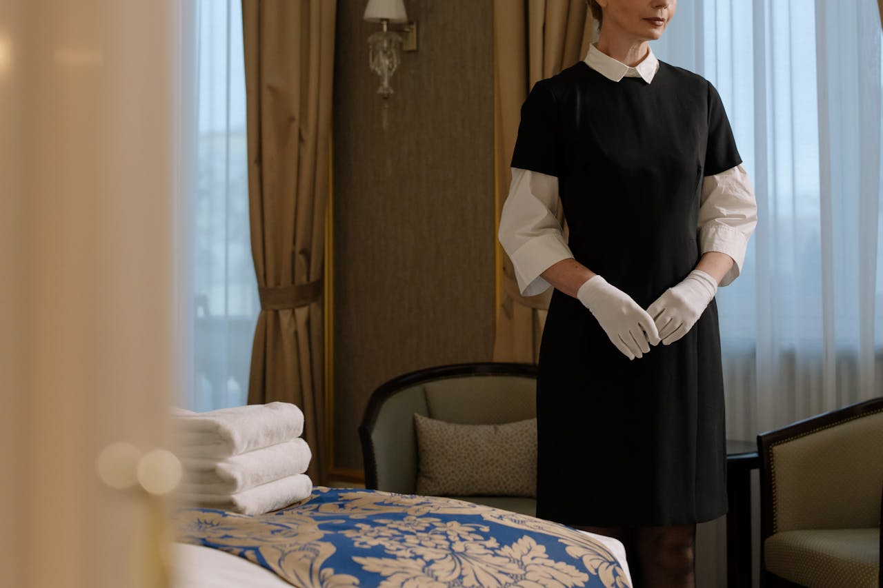 services-03 A housekeeper in uniform prepares a luxury hotel room, showcasing professionalism and service.